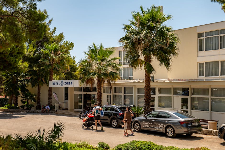Hotel Zora in Primošten, Croatia, featuring palm trees and parked cars, under a bright summer sky.