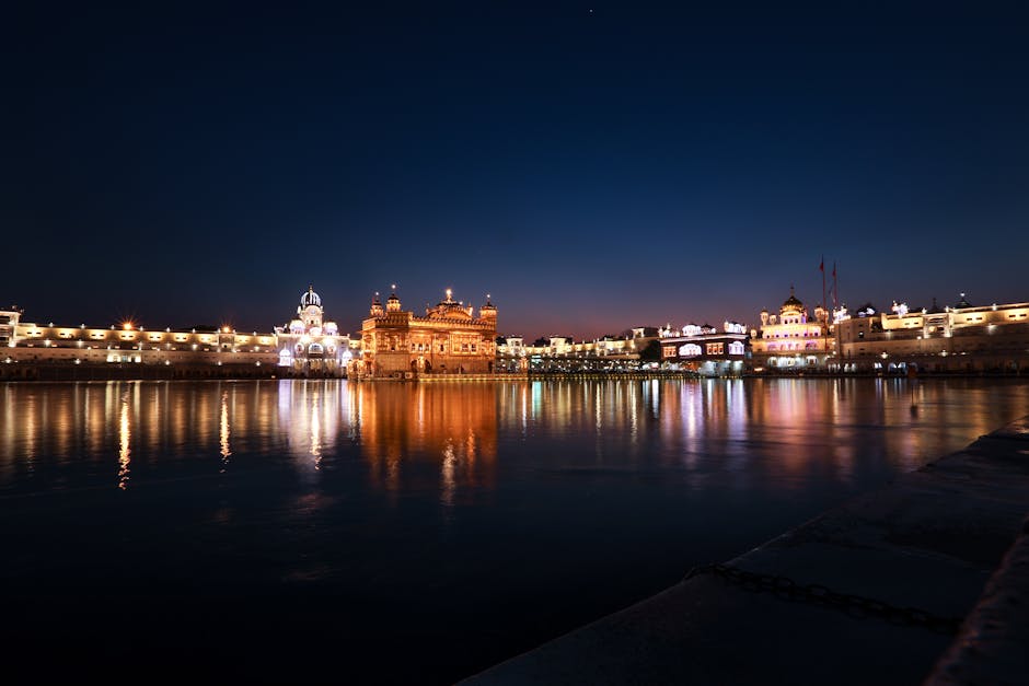 Riverbank with illuminated medieval Sikh gurdwara with fence with lights reflecting on water surface at night time in street in India