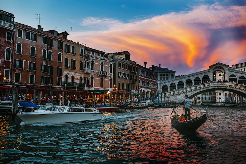 Stunning view of Venice canal at sunset with gondolas and the Rialto bridge in the background.