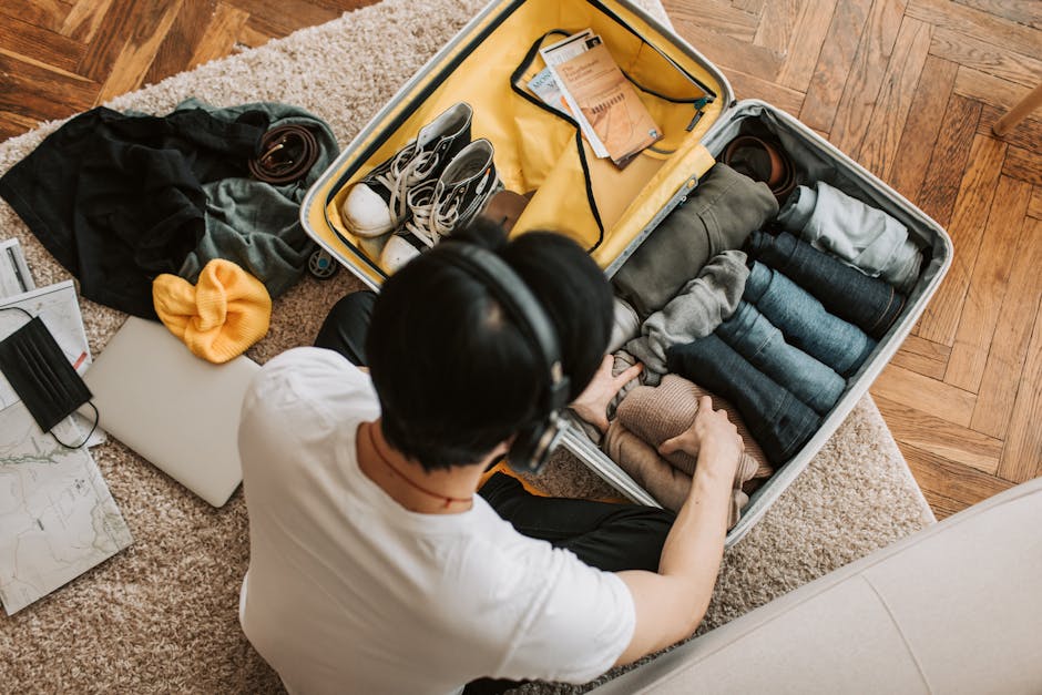 Adult packing clothes in a suitcase while listening to music at home. Overhead view on rug.