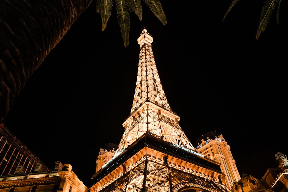 Stunning view of the illuminated Eiffel Tower replica at night in Las Vegas, with palm trees framing the shot.