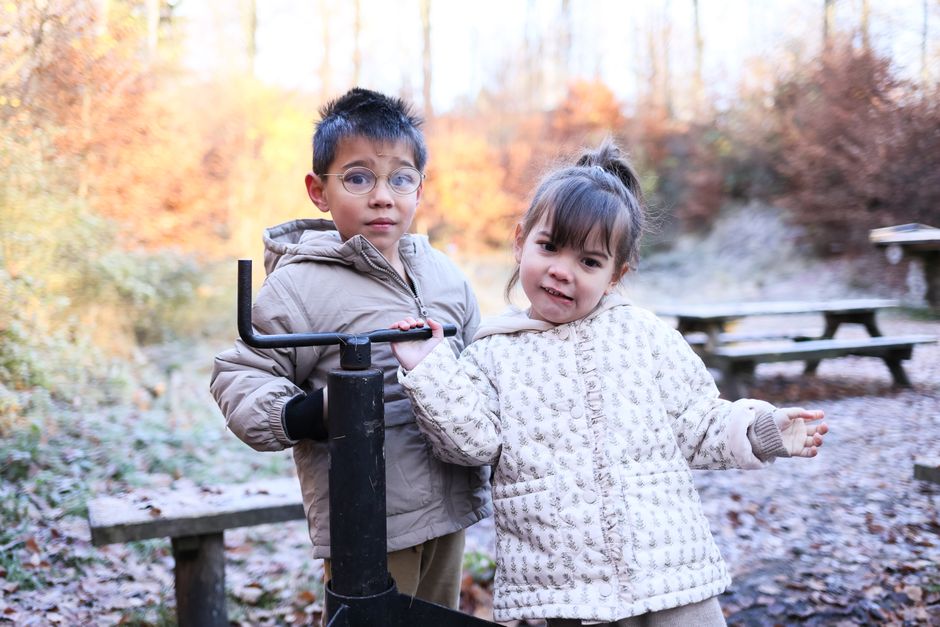 Two children enjoying a crisp autumn day outdoors with smiles and cozy coats.