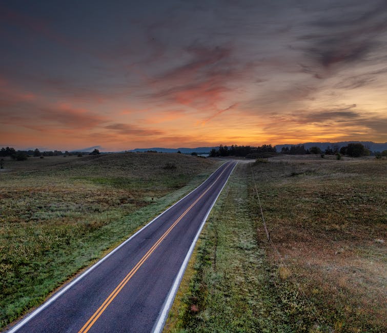 An empty rural road in West Newton, MN at dusk with vibrant sky and open fields.