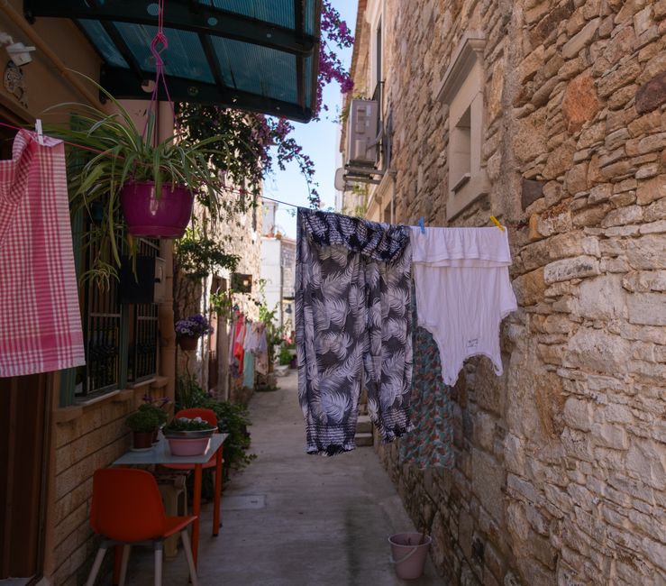 Picturesque alleyway in Foça with colorful laundry hanging between stone buildings.