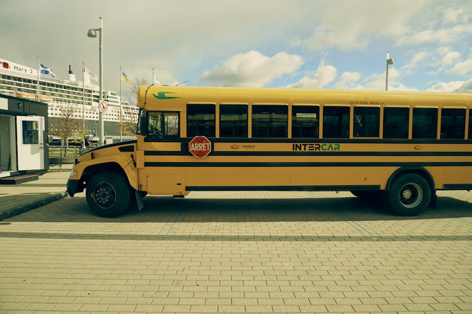 A yellow school bus parked at the Quebec City port with a cruise ship in the background.